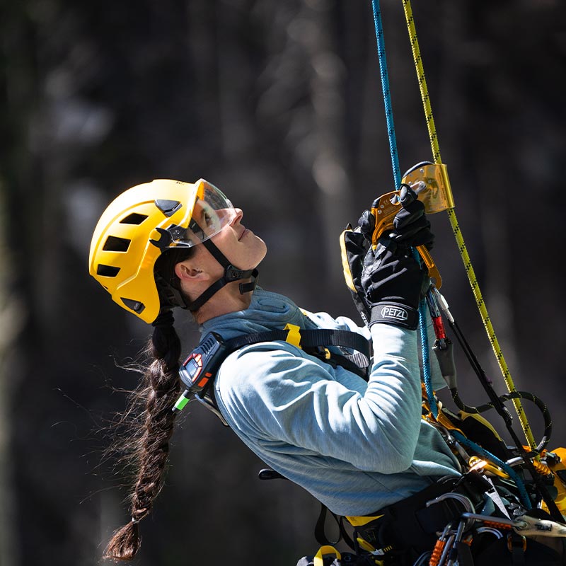 Arrampicatrice con casco giallo guarda verso l'alto lungo una via attrezzata